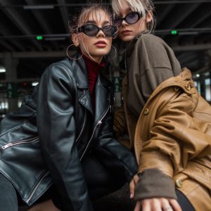 Trendy two fashion beautiful young women with stylish sunglasses in vintage leather jacket posing in the city